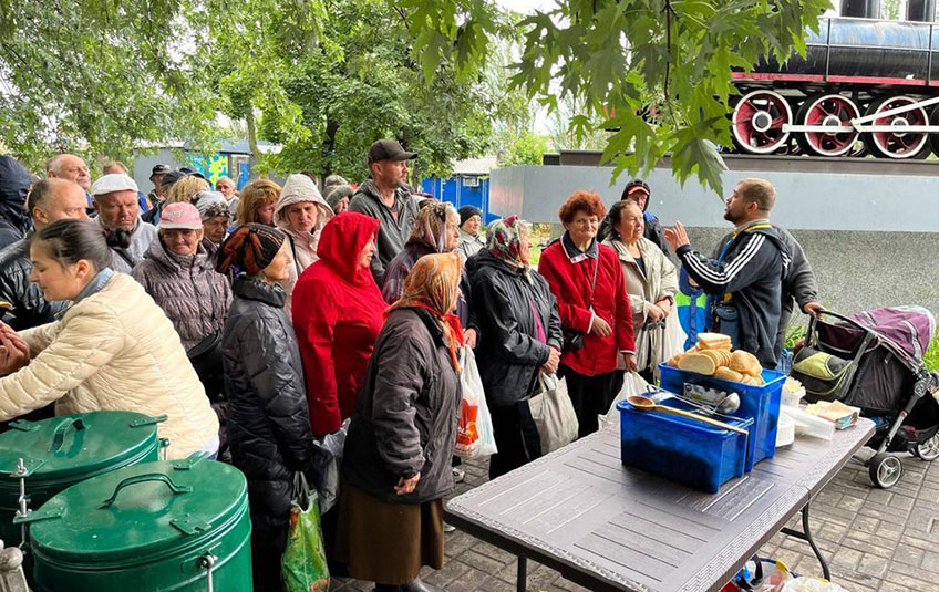 Ukrainian refugees gather around a table with food.