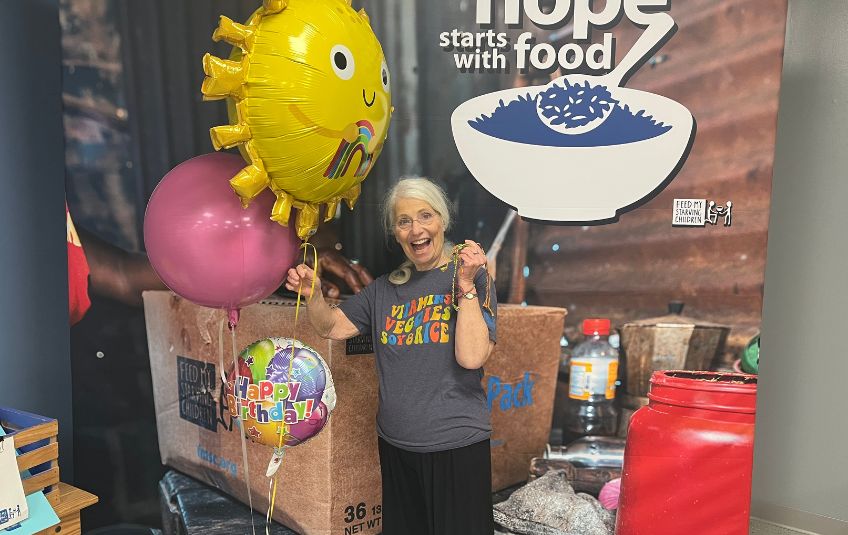 Sue Dolezal holding up MarketPlace bracelets and volunteering at FMSC Aurora. 